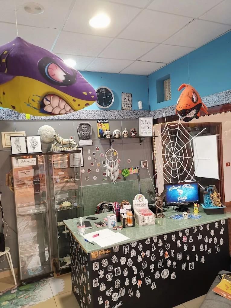 Interior de una tienda de tatuajes con mostrador de recepción, vitrina, decoración de tiburón y una computadora.