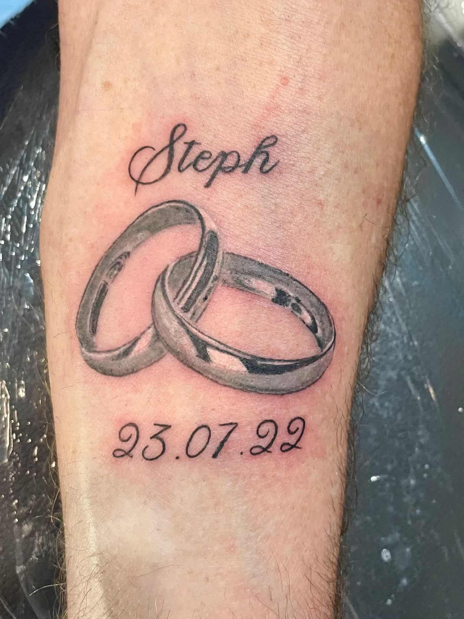 Tatuaje en el brazo que muestra dos anillos entrelazados, el nombre