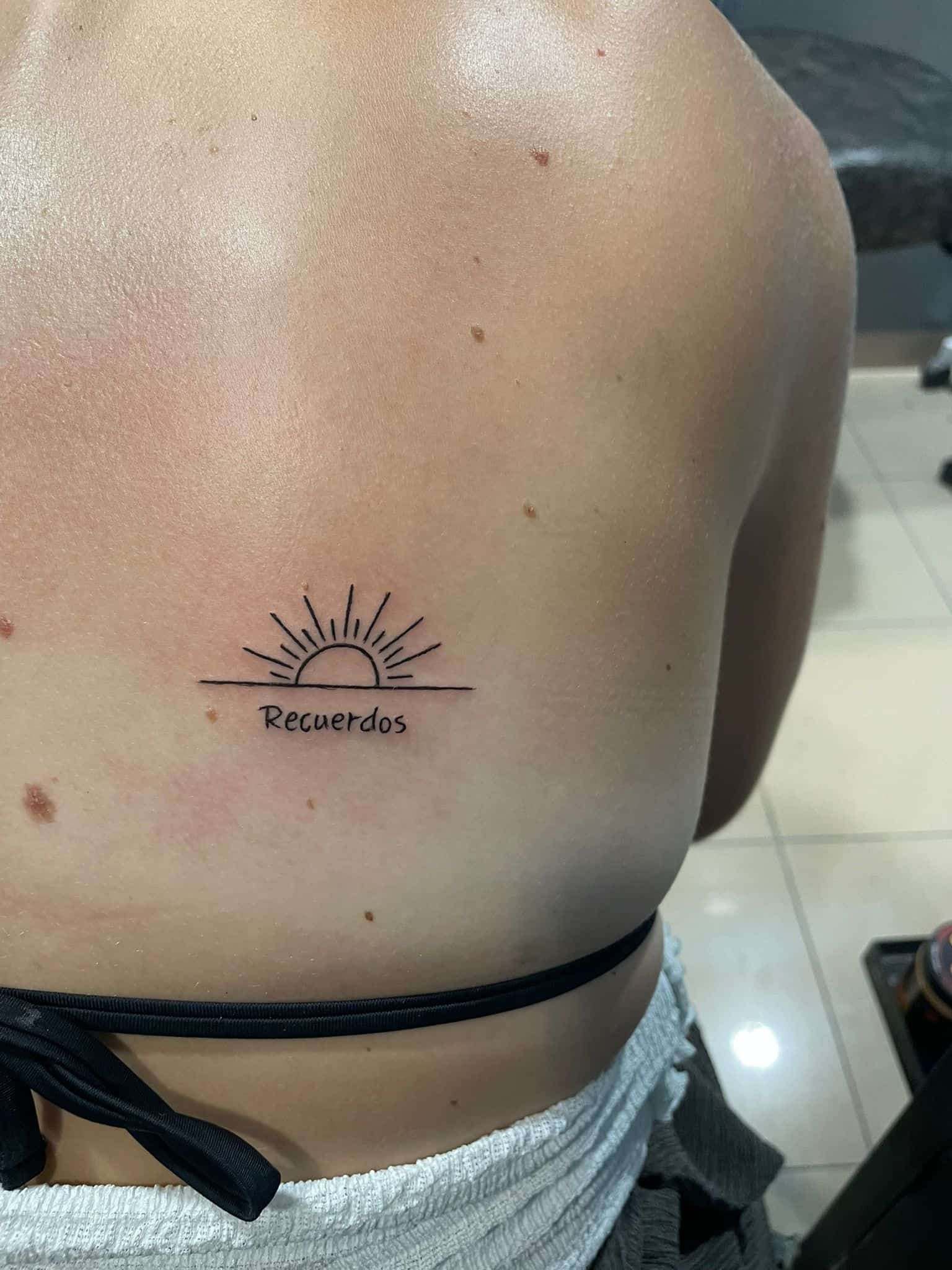 Tatuaje en la espalda que representa un amanecer con la palabra