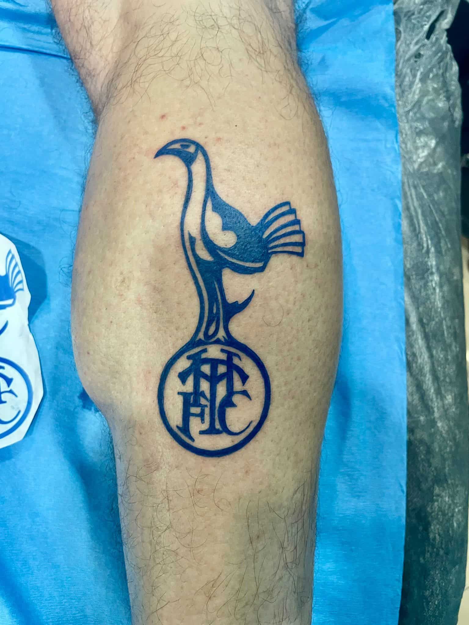 Una pierna con un tatuaje del logo del Tottenham Hotspur en tinta negra.