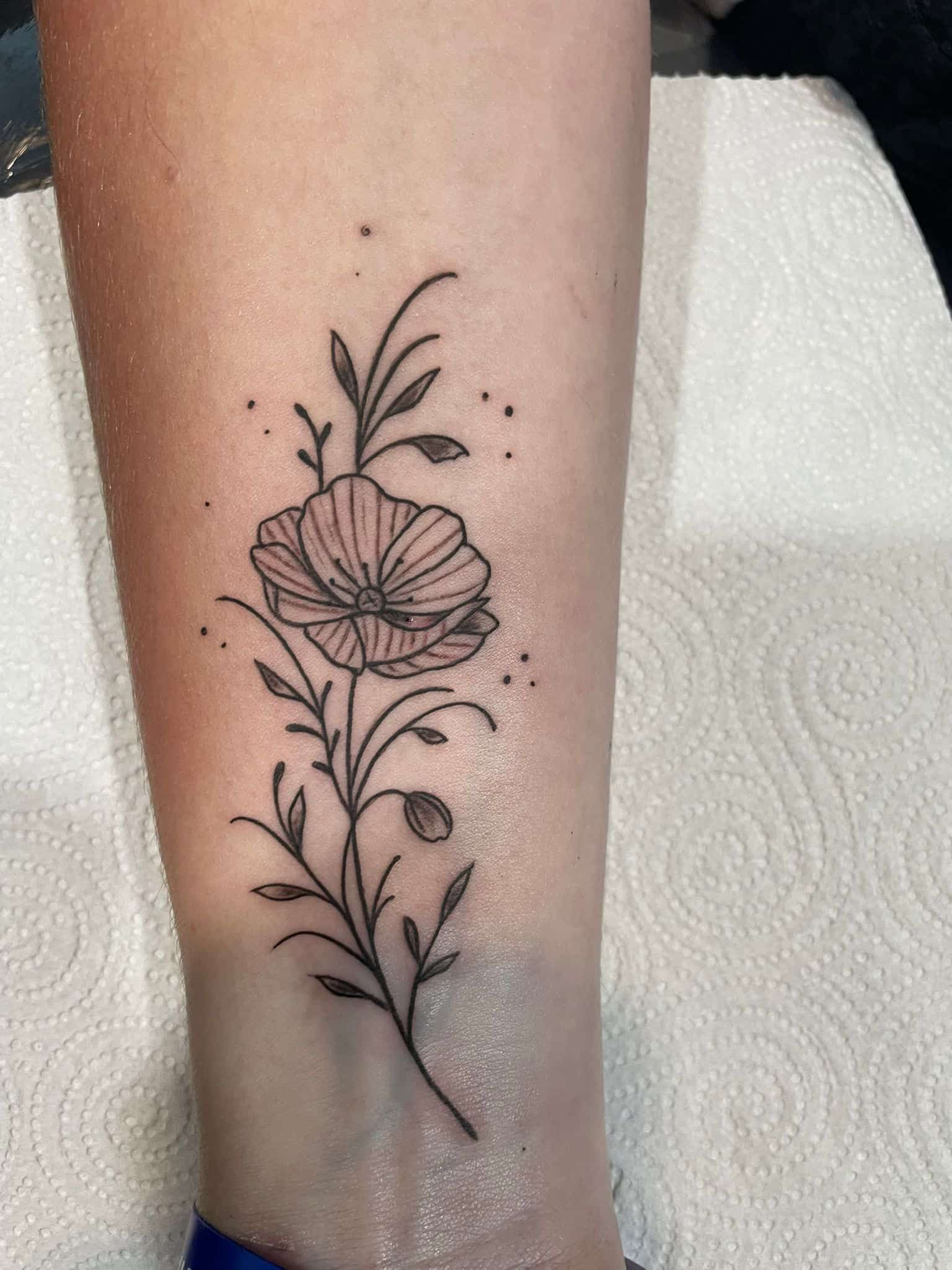 Tatuaje de flor en estilo lineal en el brazo, con hojas y pequeños puntos.