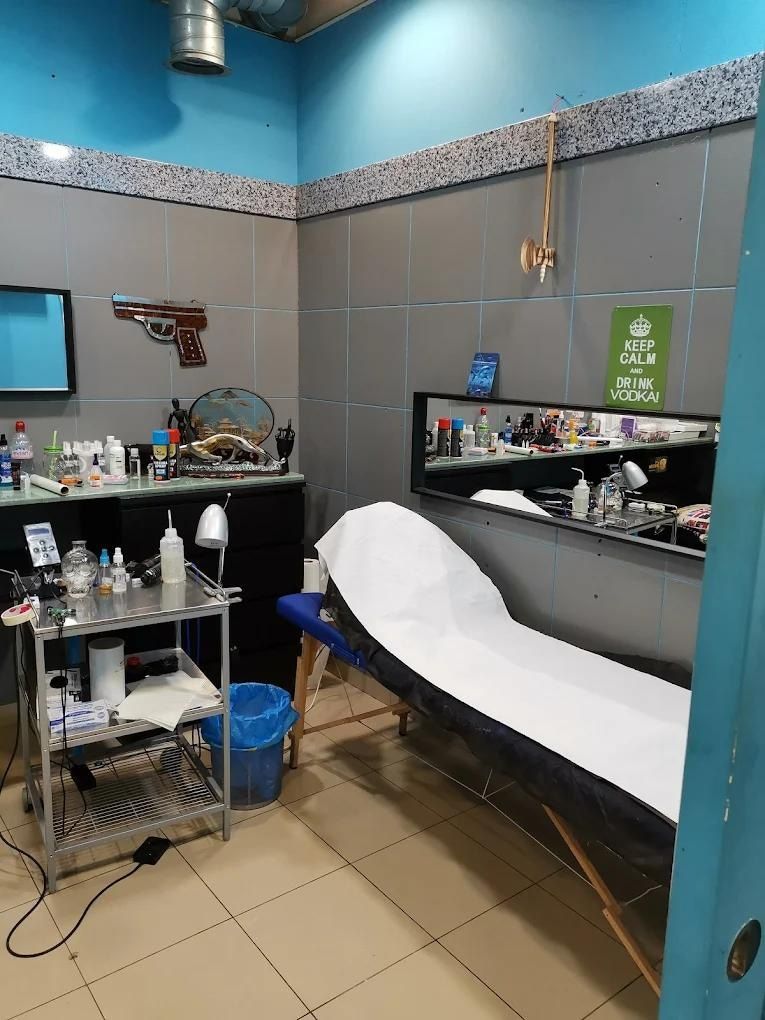 Interior de un estudio de tatuajes con mesa, equipo, silla con papel blanco y espejo. Paredes grises y azules.