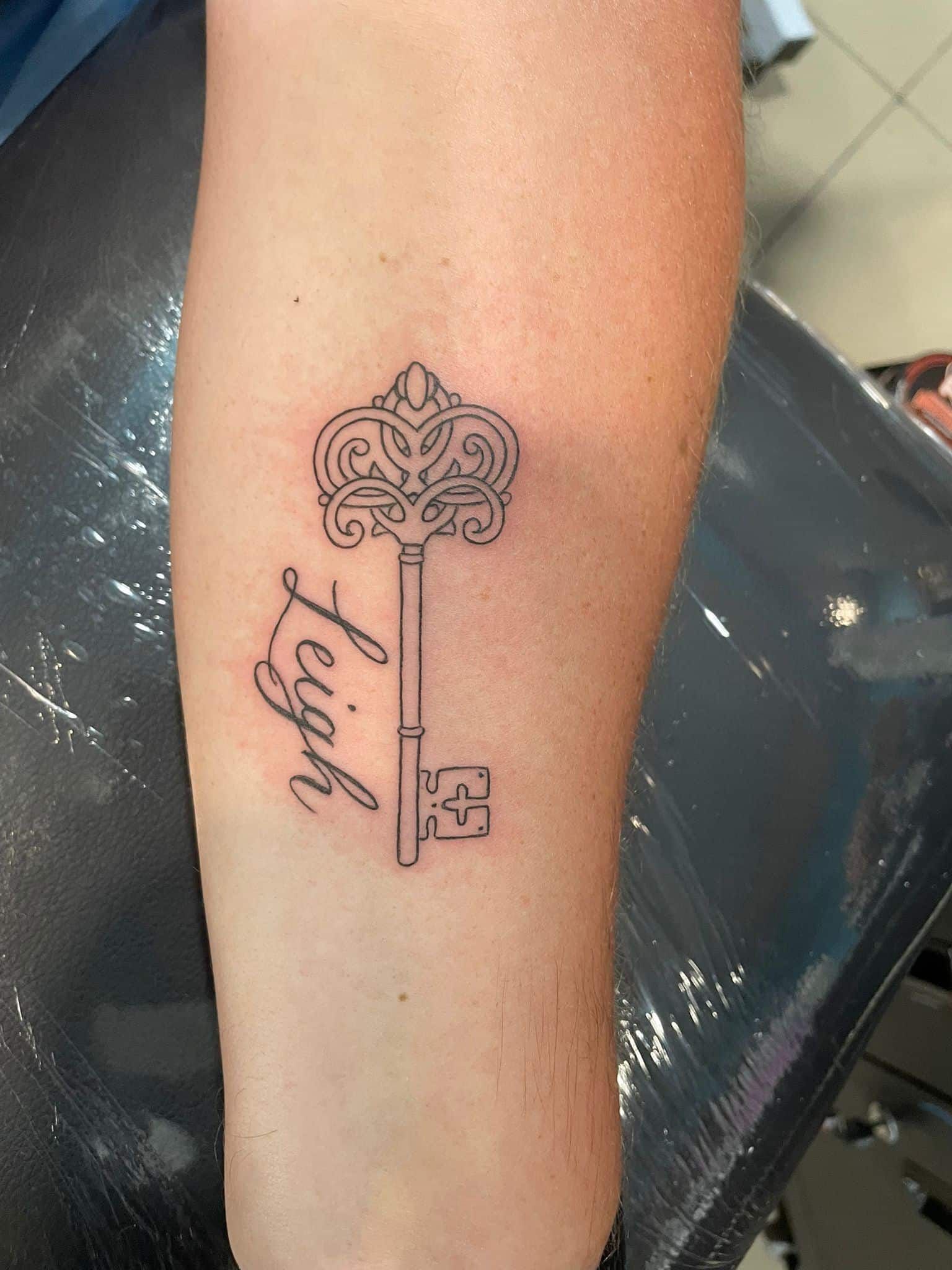 Tatuaje de una llave con la parte superior adornada y un nombre