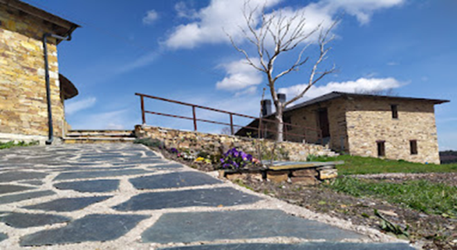 Edificios de piedra, camino y un árbol sin hojas contra un cielo azul con nubes.