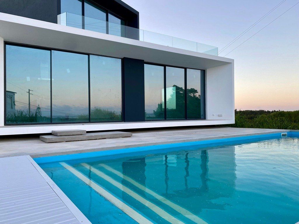 Modern huis met grote ramen die de lucht weerspiegelen, naast een blauw zwembad.