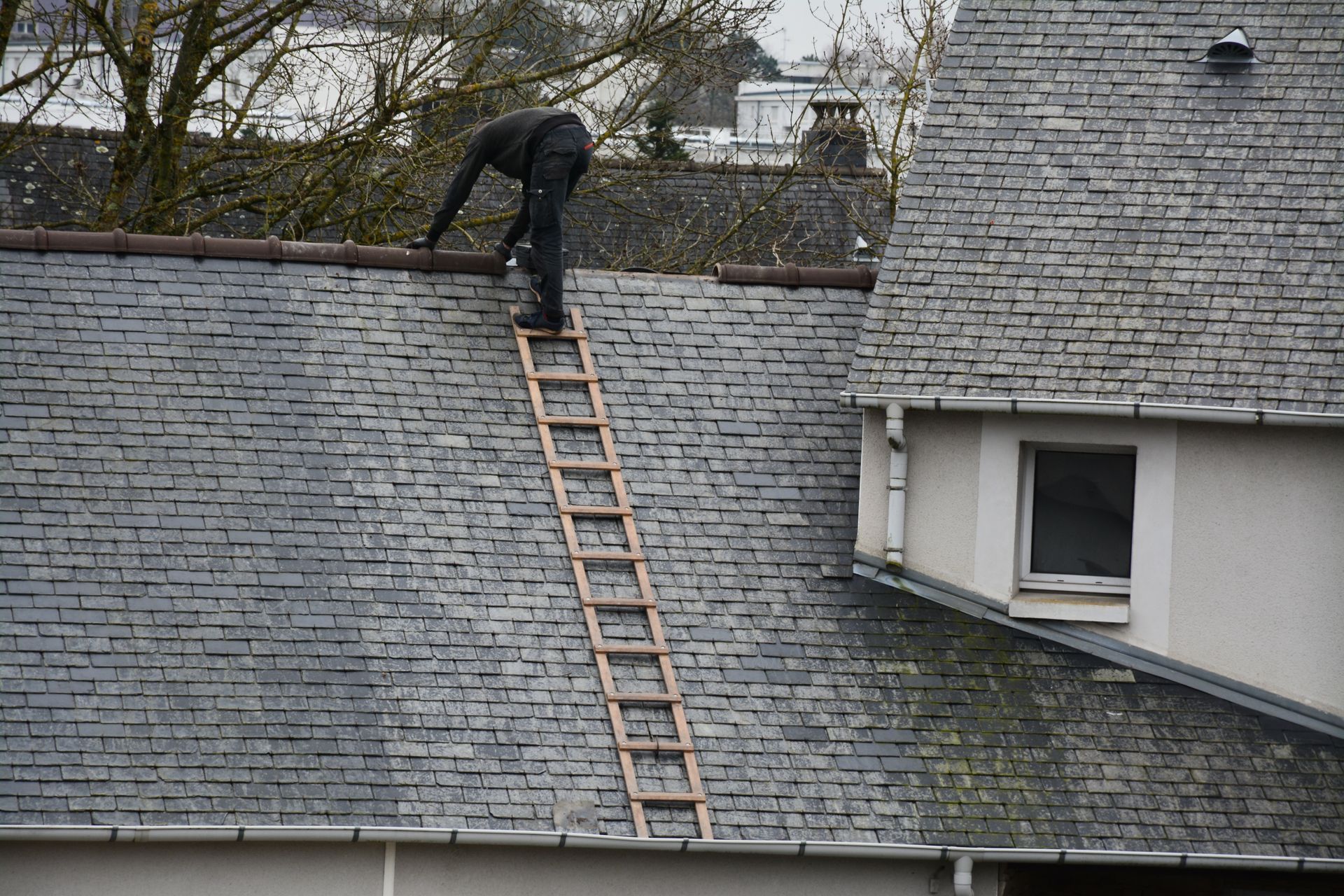 Couvreur intervenant sur la faîtière d'une toiture.
