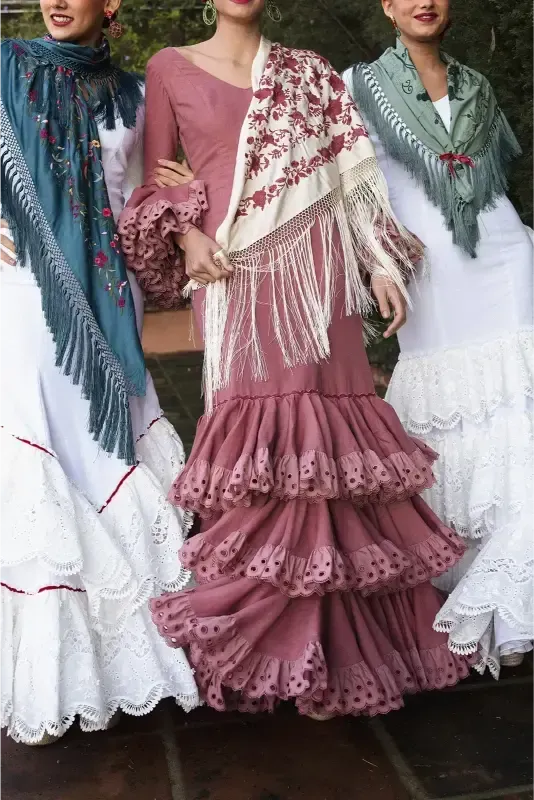 Tres mujeres con trajes de flamenca y mantones, escenario al aire libre.