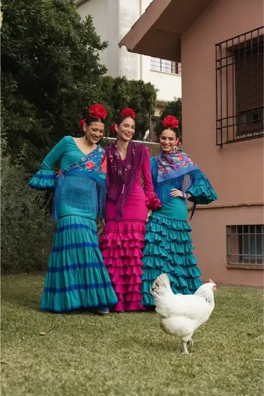 Tres mujeres con trajes de flamenca posan con una gallina en un jardín.