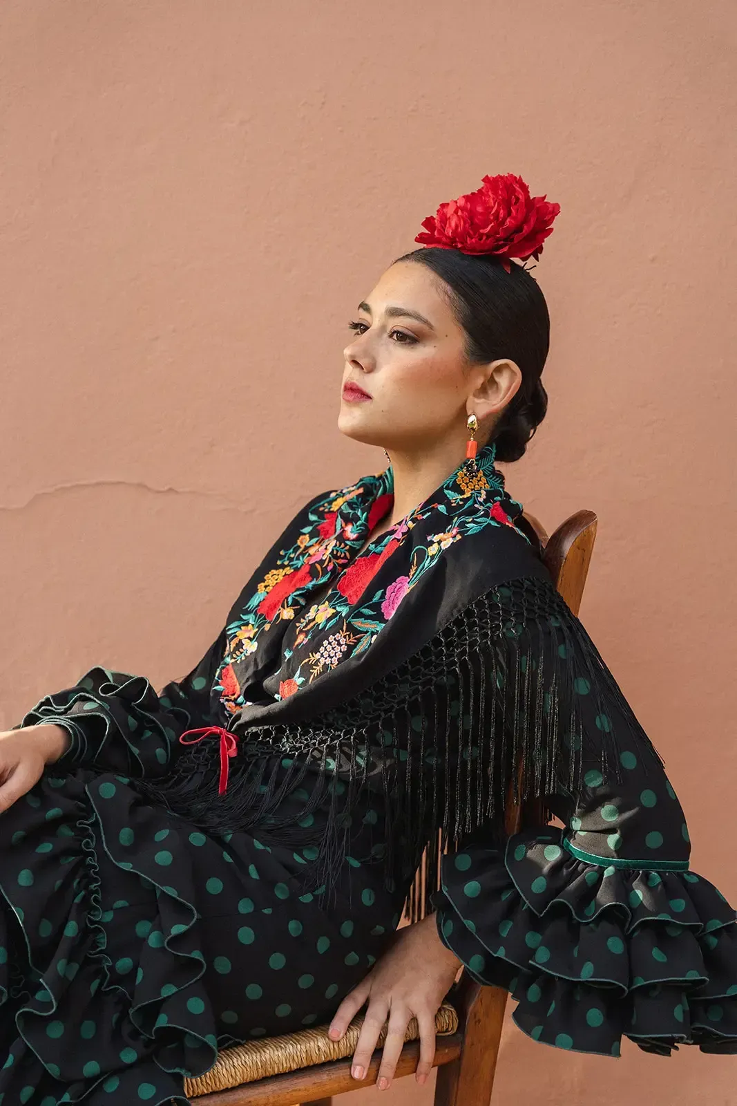 Mujer con traje de flamenca y flor roja en el pelo, sentada, mirando a la cámara.