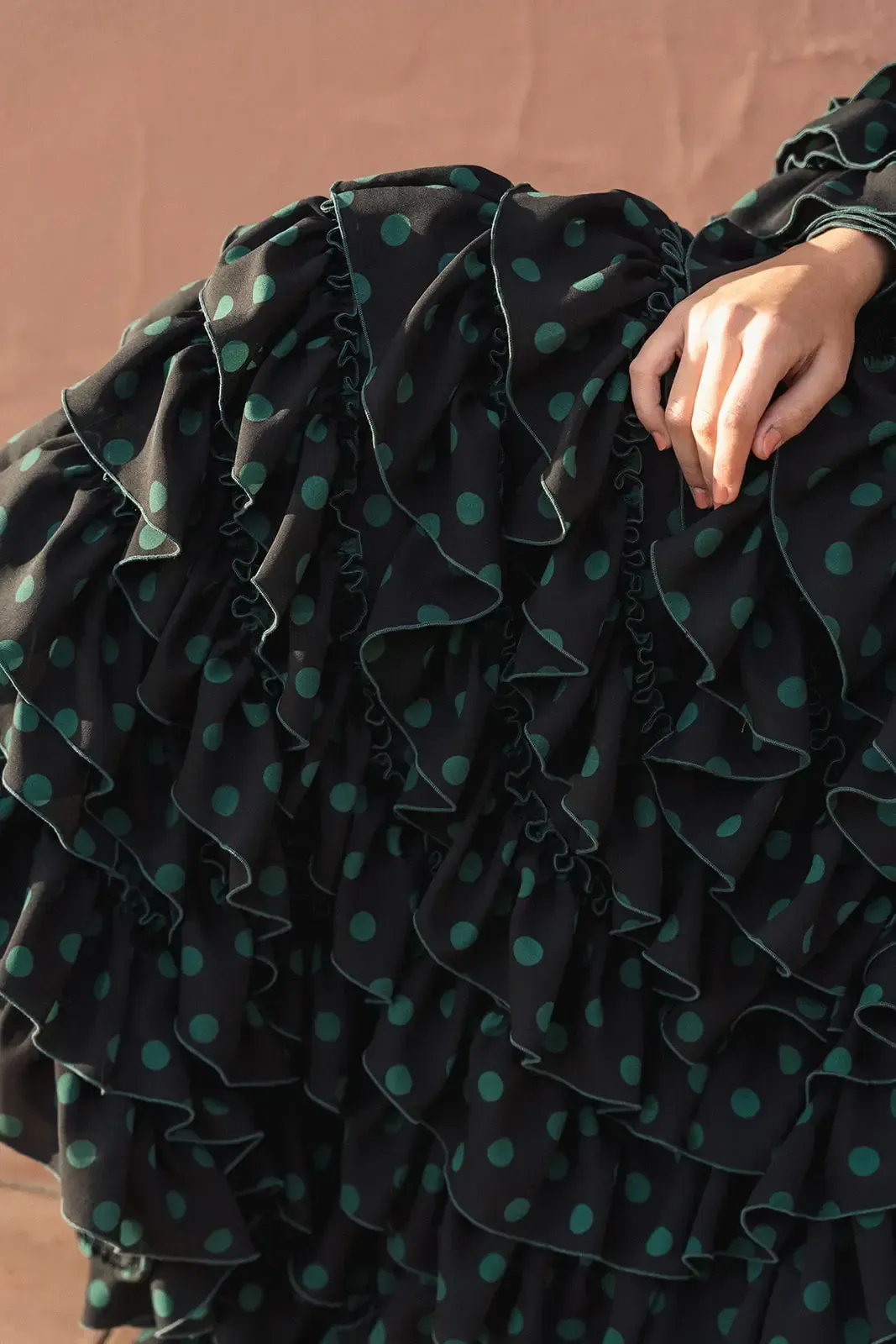 Vestido negro con lunares verdes y múltiples volantes; mano apoyada en la falda.