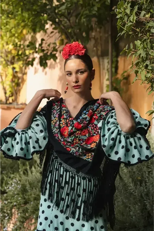 Mujer con traje de flamenca de lunares, flor roja en el pelo, al aire libre.