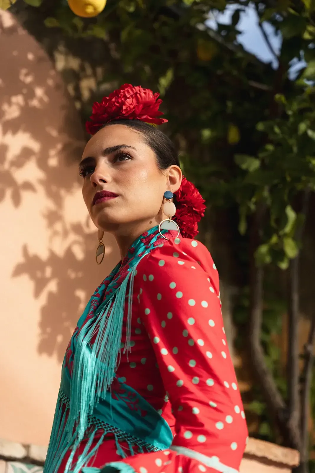 Mujer con vestido de lunares rojos, chal verde azulado y flor en el pelo, exterior.