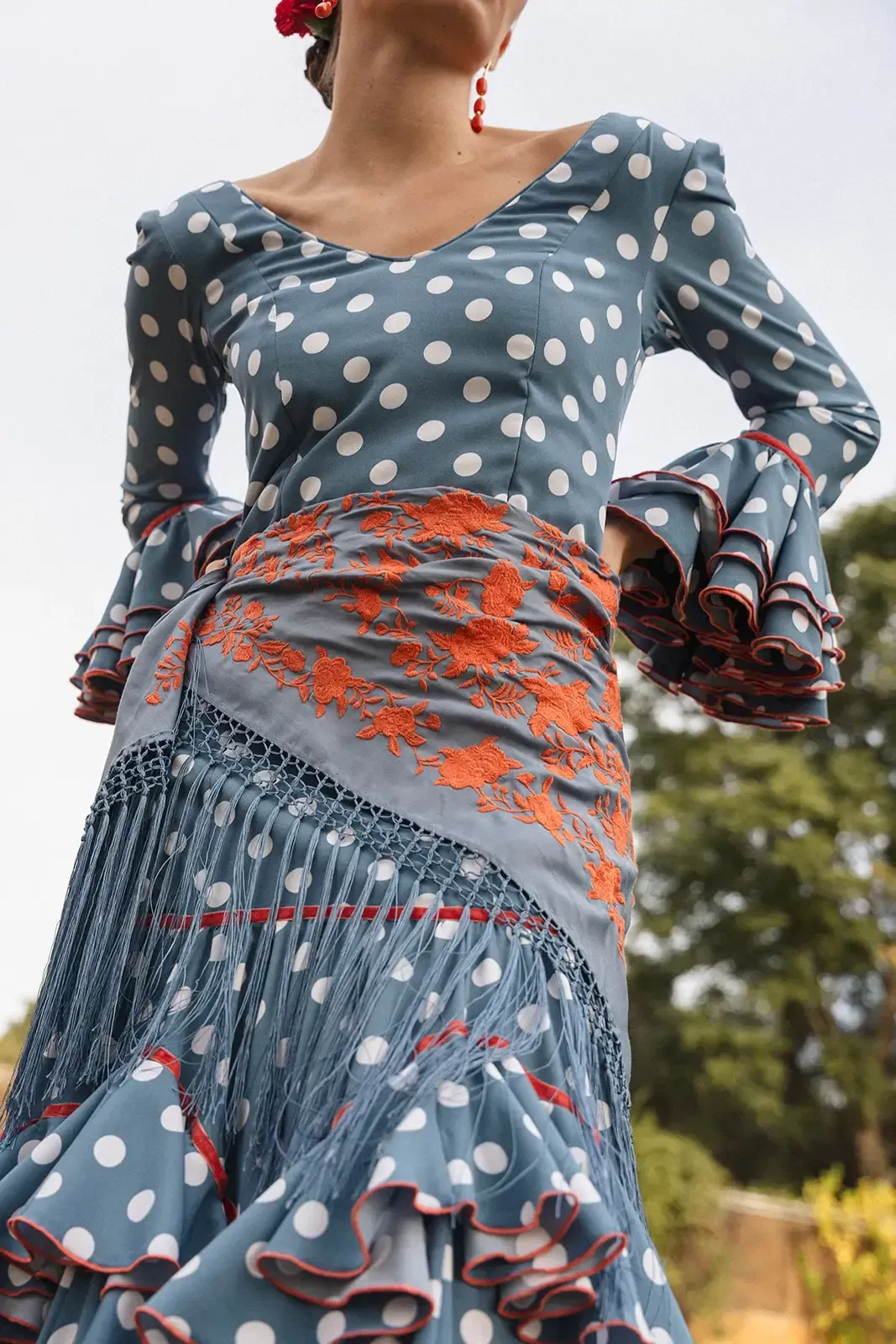 Mujer con traje de flamenca de lunares azules y ribete rojo, con chal y complemento floral para el pelo.