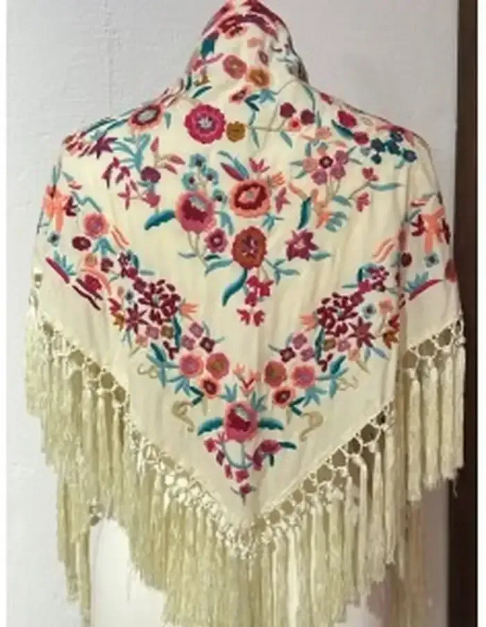 Chal bordado de color crema con diseño floral colorido y flecos largos.