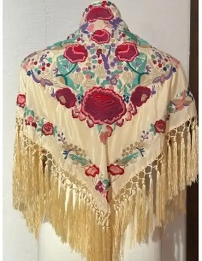 Chal de color crema con grandes flores bordadas en tonos rojos y rosas, hojas verdes y flecos largos.