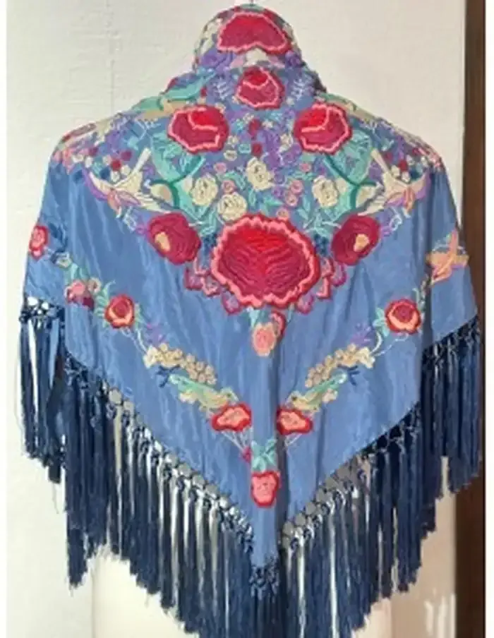 Chal de seda azul con intrincado bordado floral en rosa y verde, bordes con flecos.