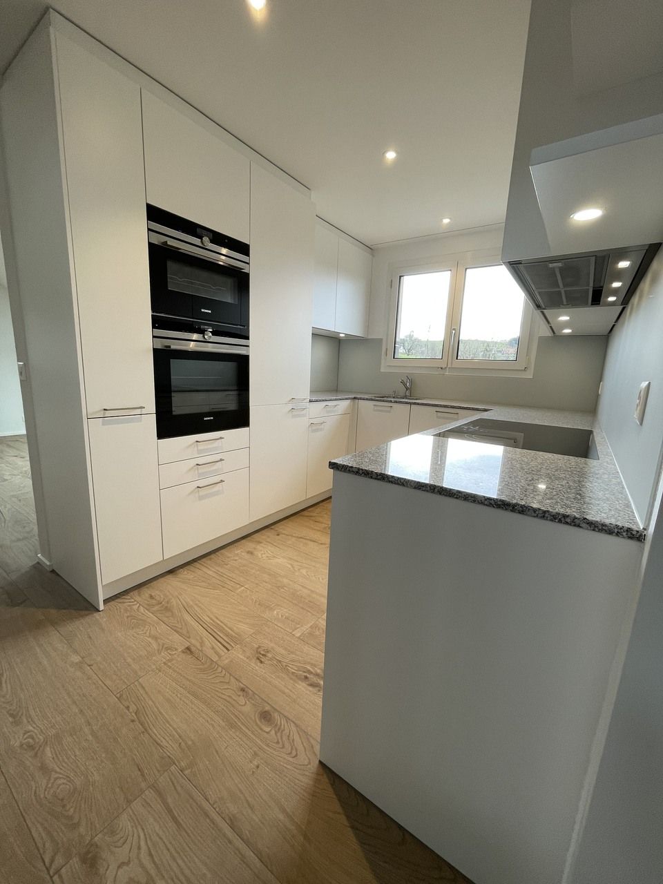 Eine Küche mit weissen Schränken und Granit-Arbeitsplatten. Foto von der RRB GmbH