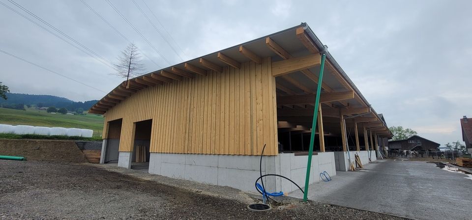 An einer Schotterstrasse wird ein Holzgebäude mit Metalldach errichtet. Foto von der RRB GmbH