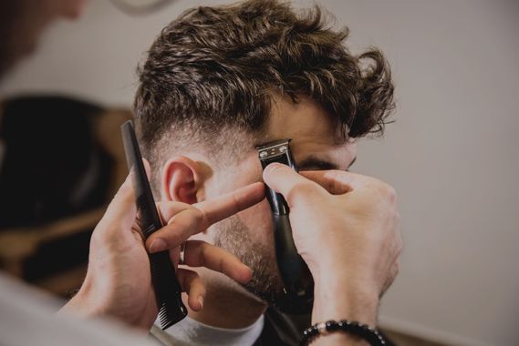 Ein Friseur schneidet einem Kunden die Haare in einem modernen Salon mit geometrischen Deckenleuchten.