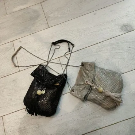 Una bolsa negra y una bolsa plateada están sobre un piso de madera.