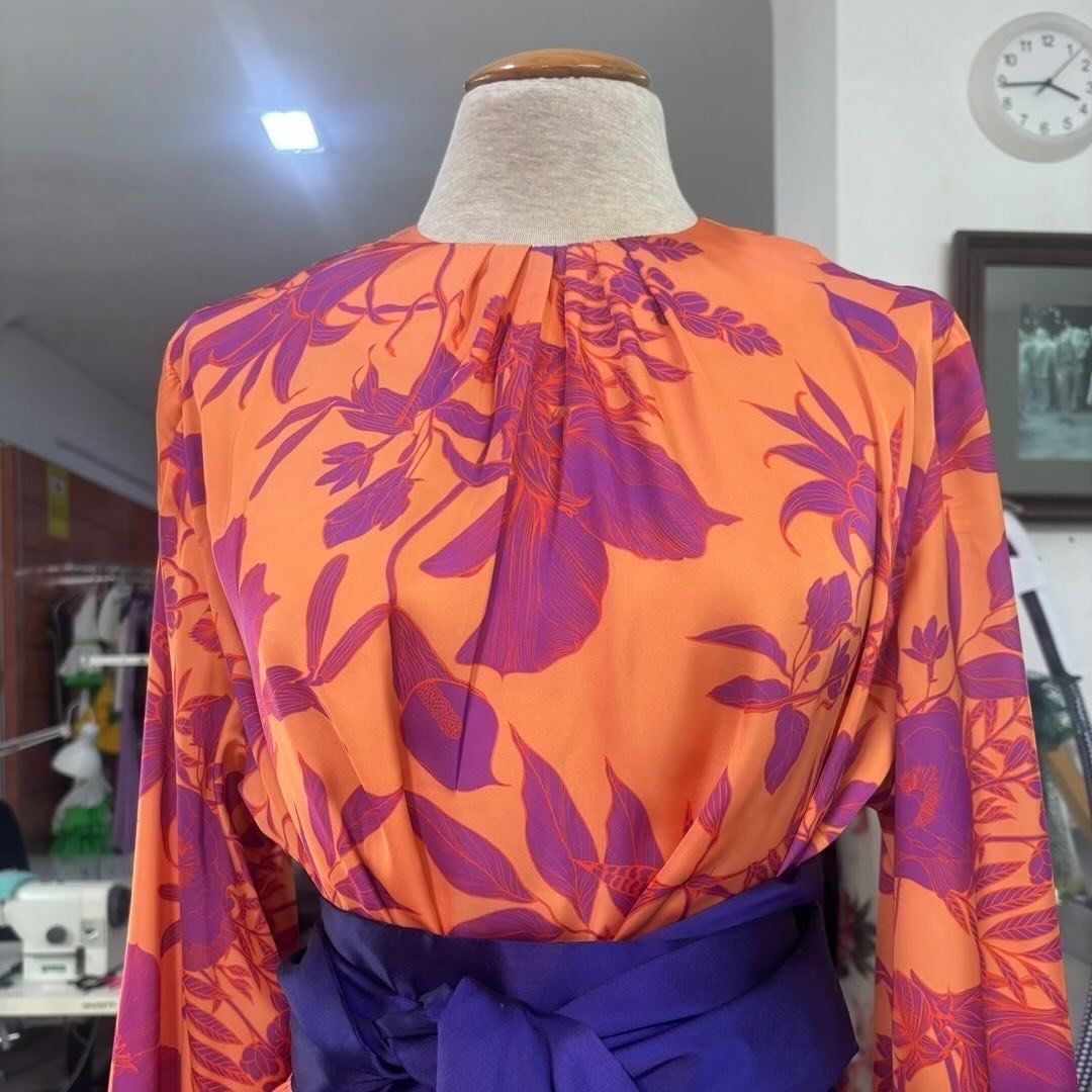 Blusa naranja con estampado floral morado sobre maniquí, con cinturón morado.