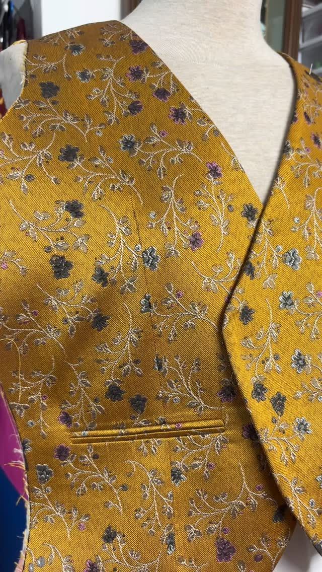 Chaleco bordado en oro sobre un maniquí. Presenta pequeñas flores azules, hilo dorado y un bolsillo.