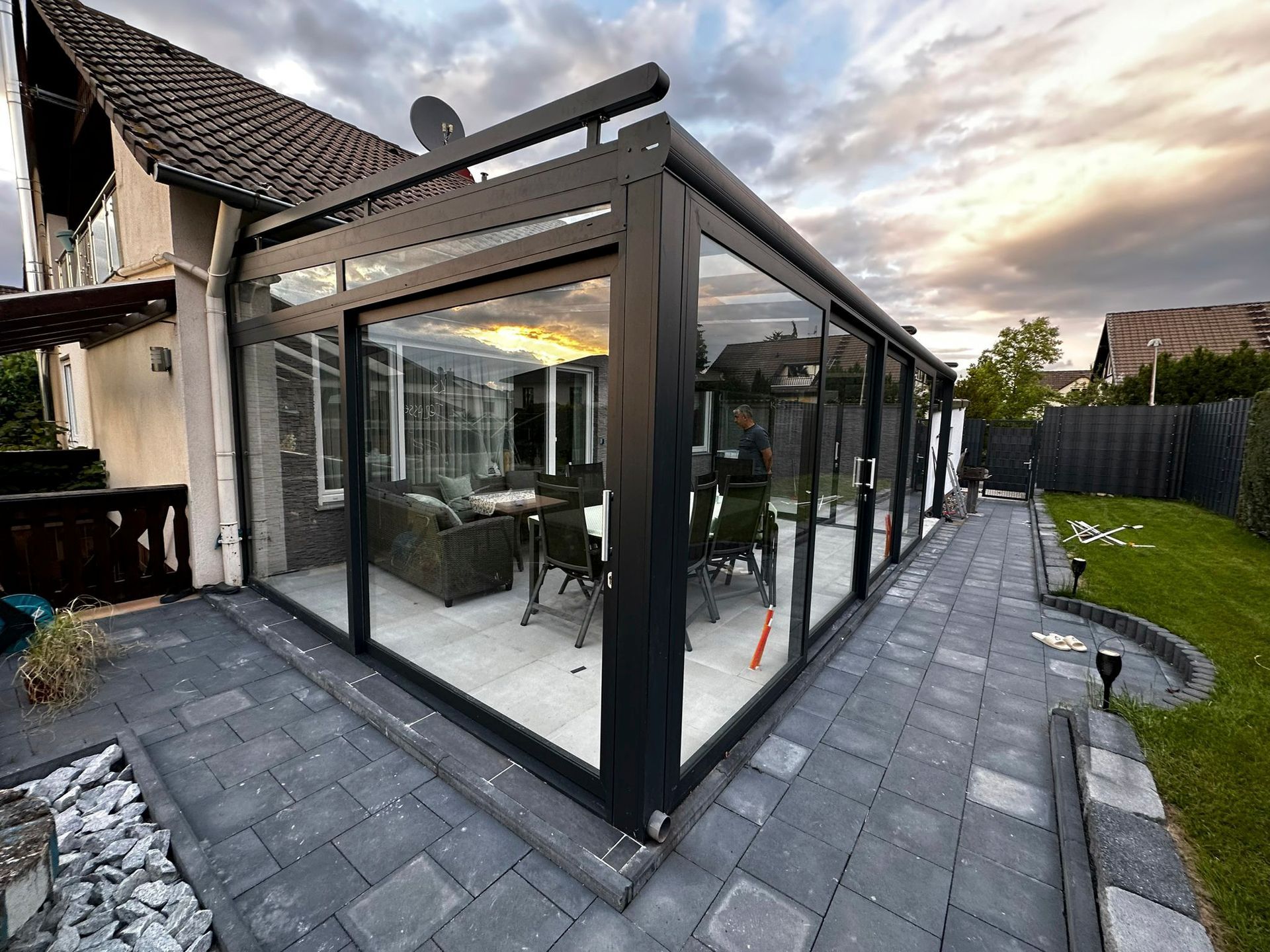 Ein großer Glasraum mit vielen Fenstern und einer Terrasse vor einem Haus.