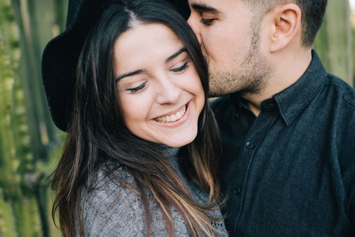 Un couple souriant en extérieur, l'homme embrassant le front de la femme au milieu de la verdure.