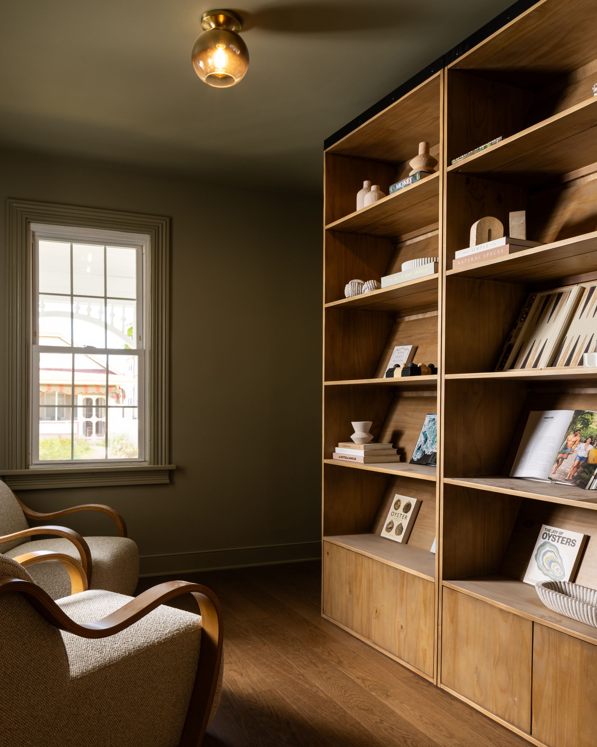 Cozy reading nook with woven chairs, wooden bookshelf, and a window in warm brown tones
