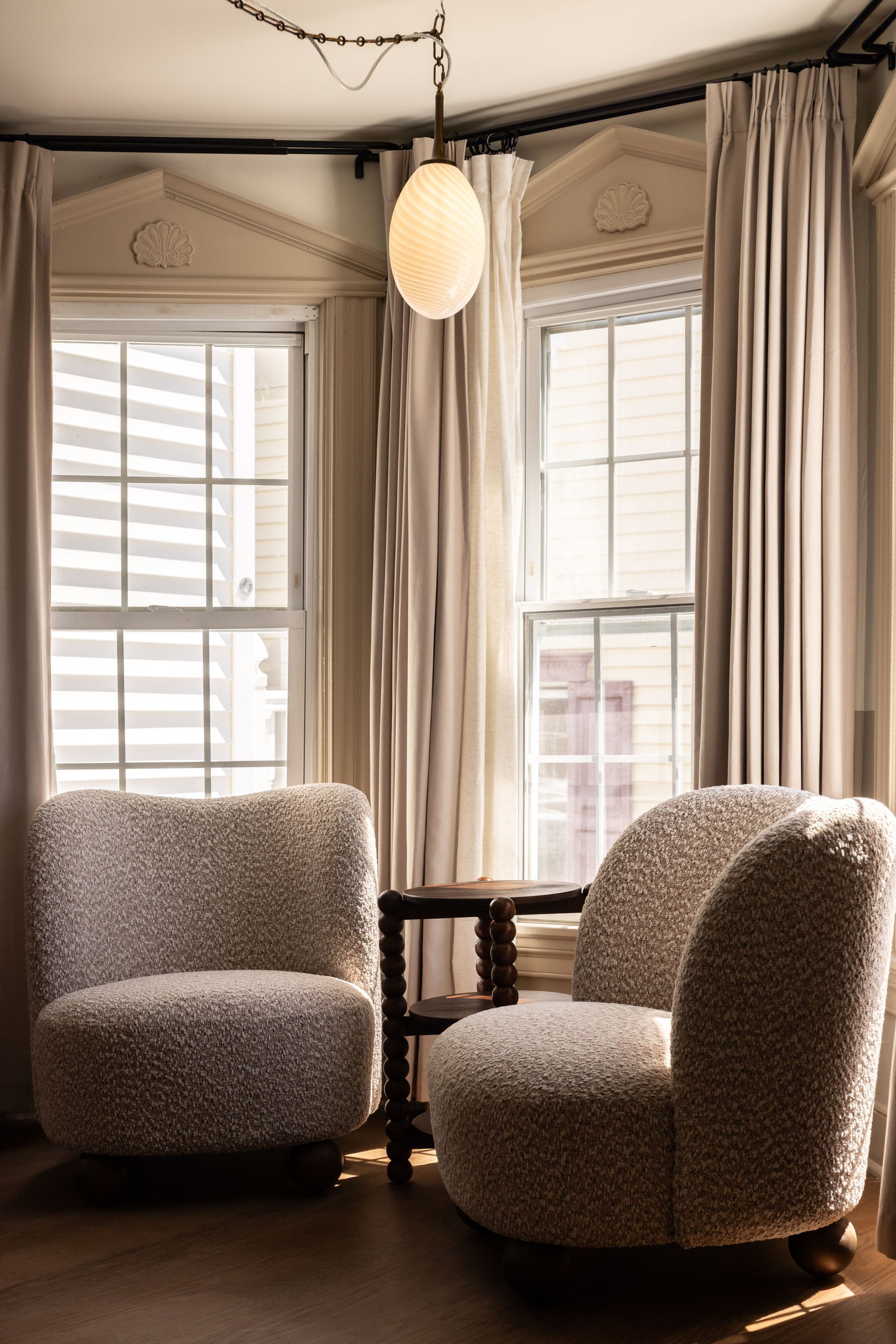 Two textured armchairs by tall windows in a cozy beige sitting room