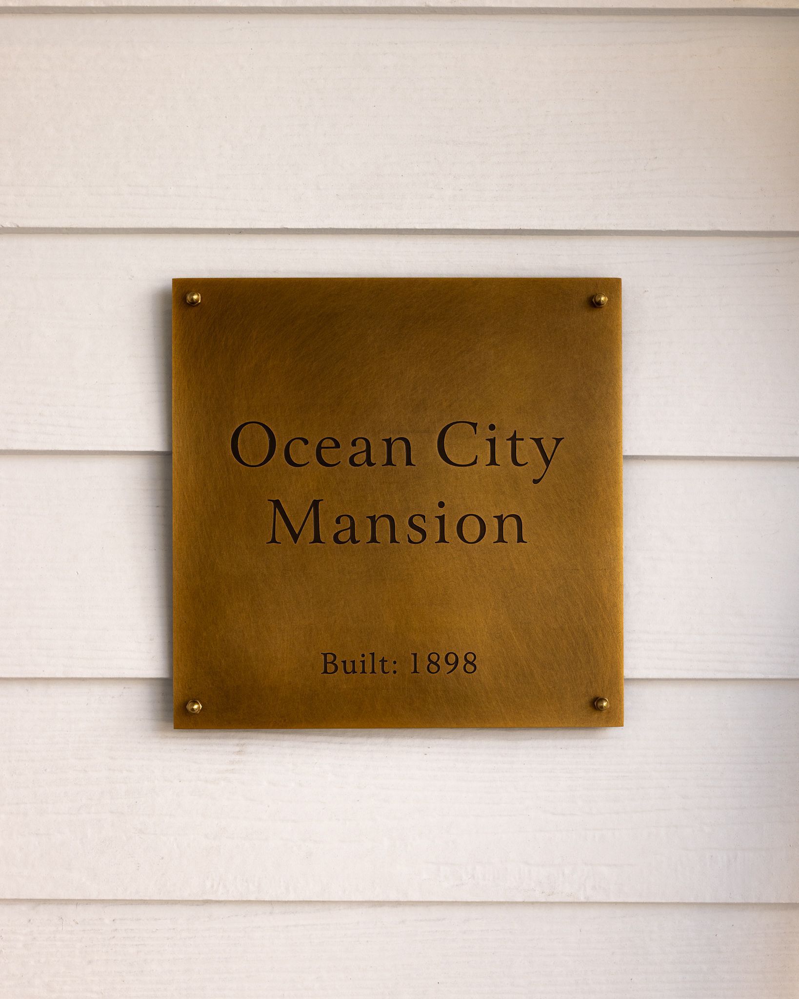 Brass plaque reading “Ocean City Mansion” on white siding, built 1896.