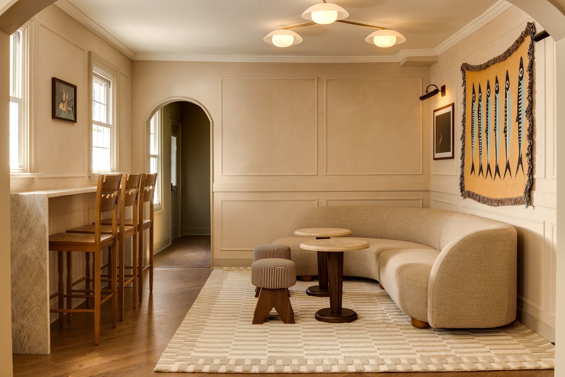 Cozy beige living room with arched doorway, window nook, round table, and woven wall hanging
