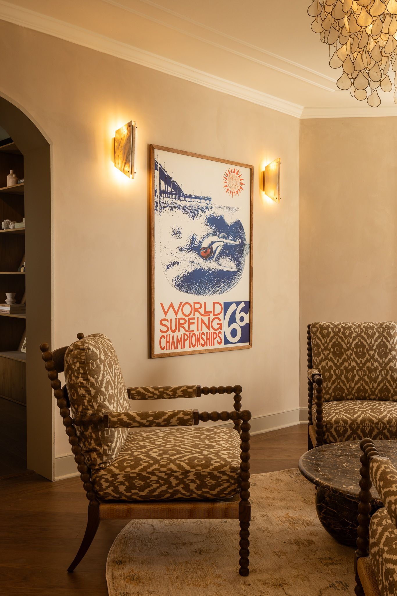 Elegant living room with patterned chairs, glass table, wall sconces, and framed artwork on a beige wall