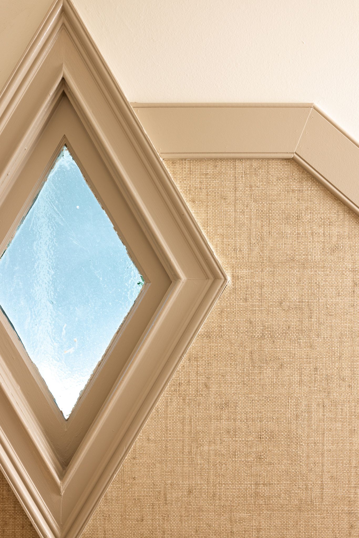 Beige wall with a diamond-shaped window showing blue sky and textured wallpaper panel