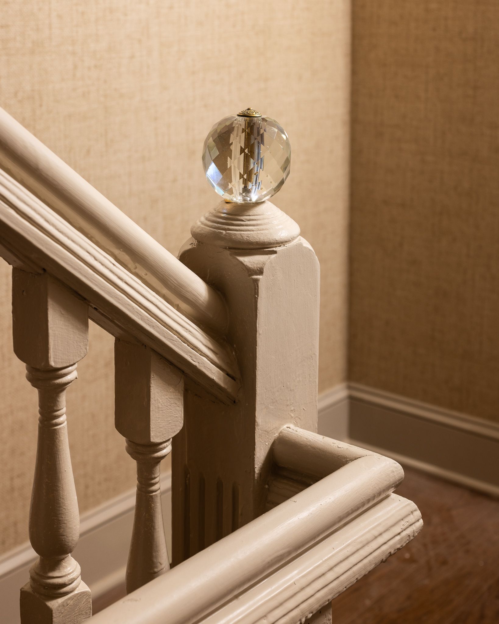 Wooden staircase banister with a crystal knob in a beige interior.