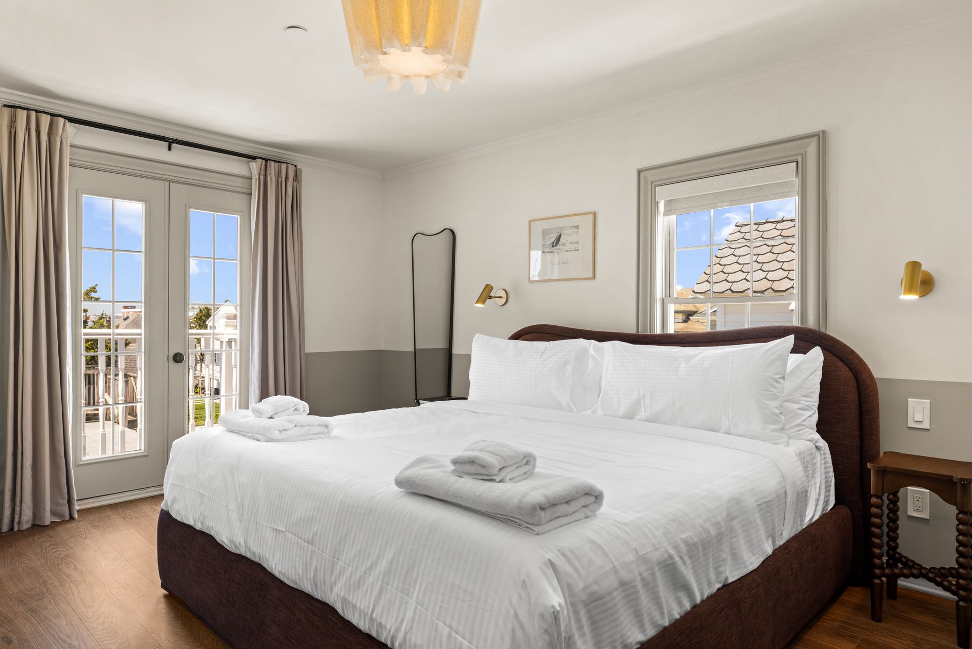 Cozy beige bedroom with a bed, bedside lamp, chair, and large window overlooking the sea
