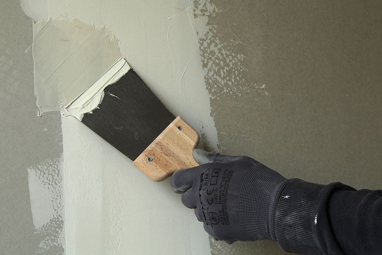 Homme qui étale des bandes de Placo à l'aide d'une spatule