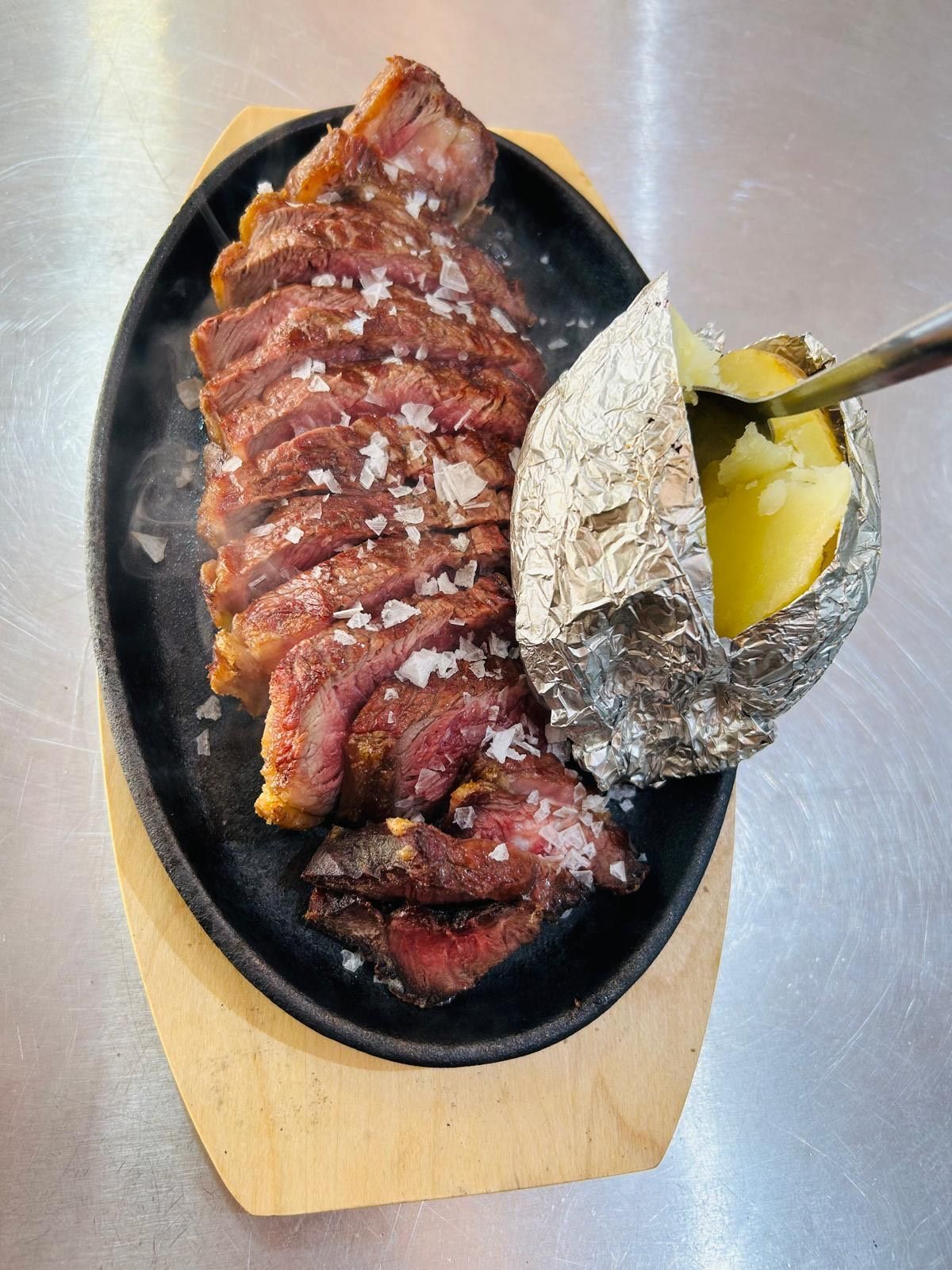 Filete cortado en rodajas con sal gruesa y patata asada sobre tabla de madera.