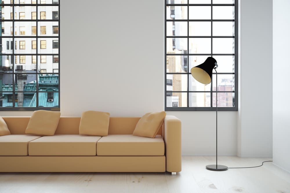 Una sala de estar con un sofá y una lámpara frente a una ventana.