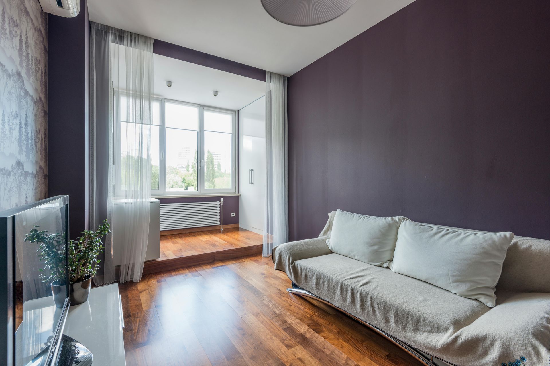 Una sala de estar con sofá, televisión y paredes moradas.