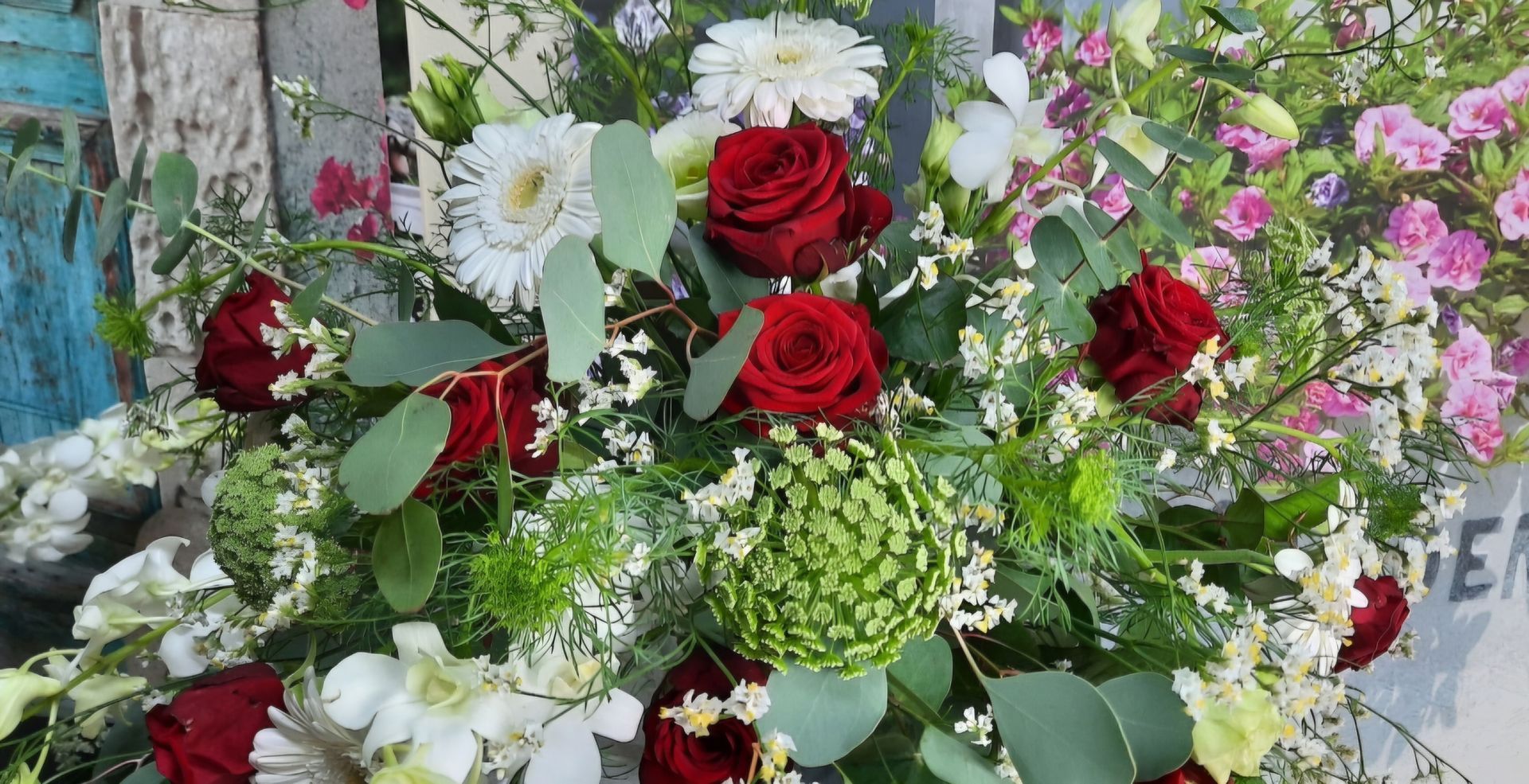 Herzförmiges Blumenarrangement; rote Rosen in der Mitte, umgeben von weißen Rosen und Grünzeug, zusammengebunden mit einem weißen Band.