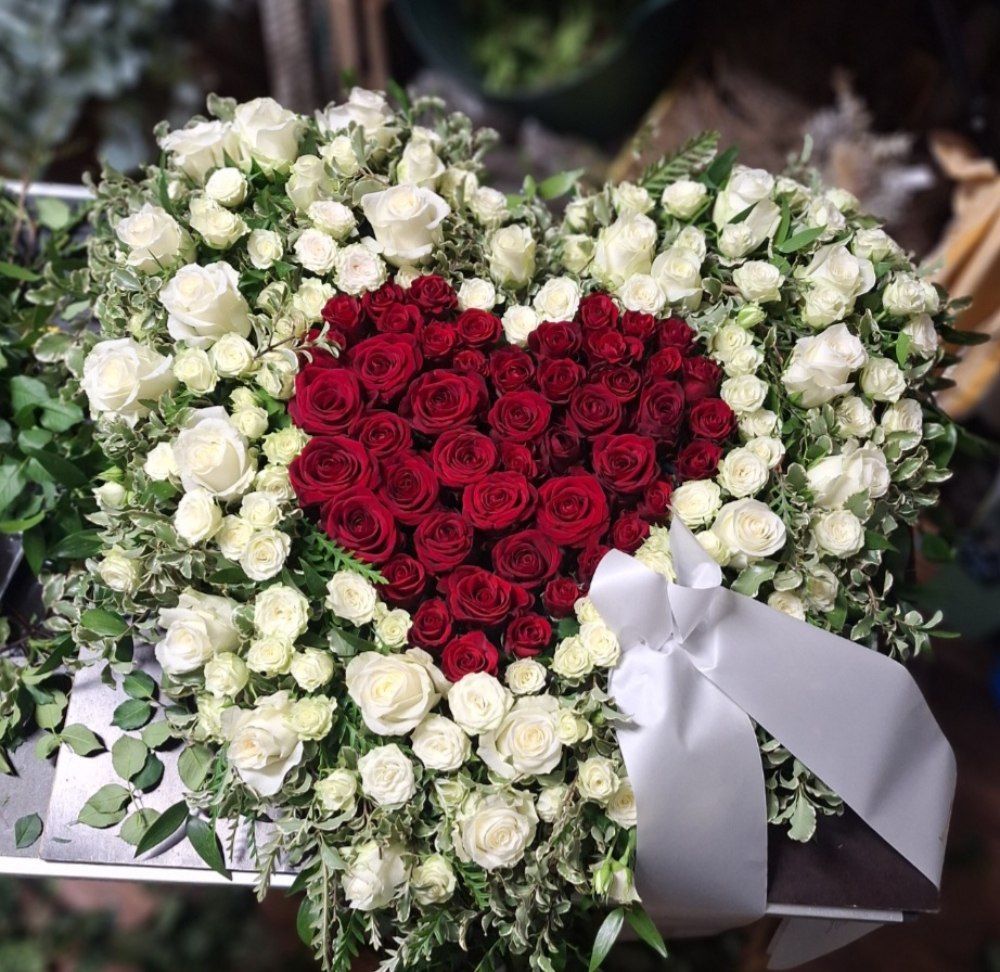 Weiße Urne, umgeben von bunten Blumen, darunter Rosen und Nelken, wahrscheinlich zu Gedenkzwecken.
