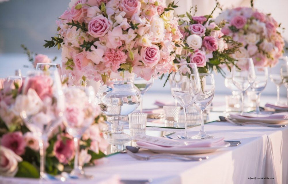 Elegante Tischdekoration für eine Hochzeit mit rosa Blumenarrangements, Kristallgläsern und weißer Tischdecke.