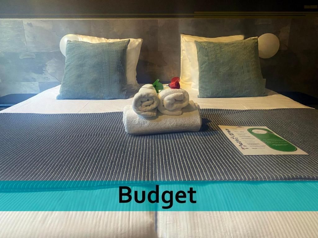 Een hotelkamer met een bed, kussens, handdoeken en een bordje met de tekst 'budget'.