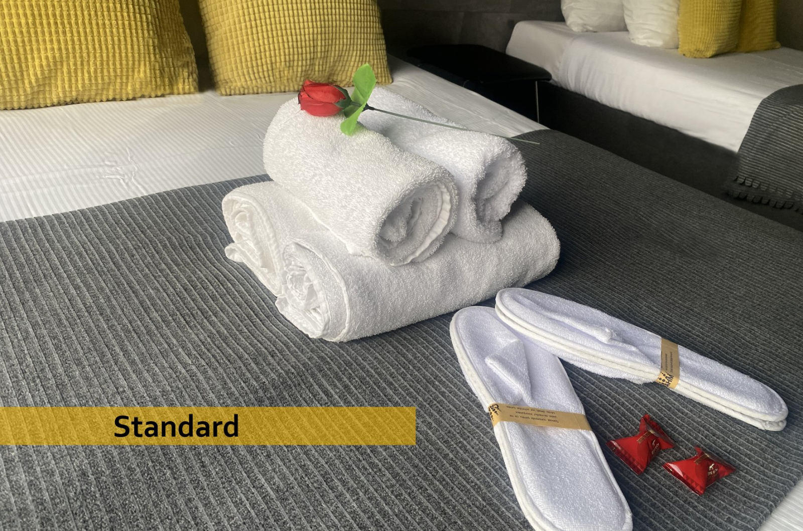 A bed with towels , slippers and a rose on it.