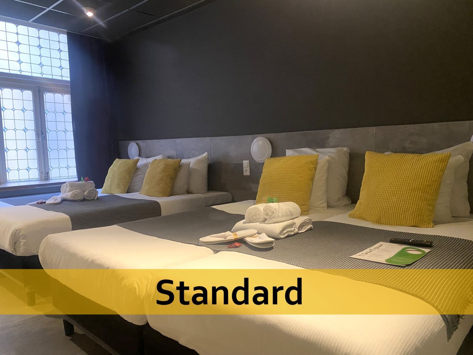 Een hotelkamer met drie bedden en een bordje met de tekst 'standaard'.