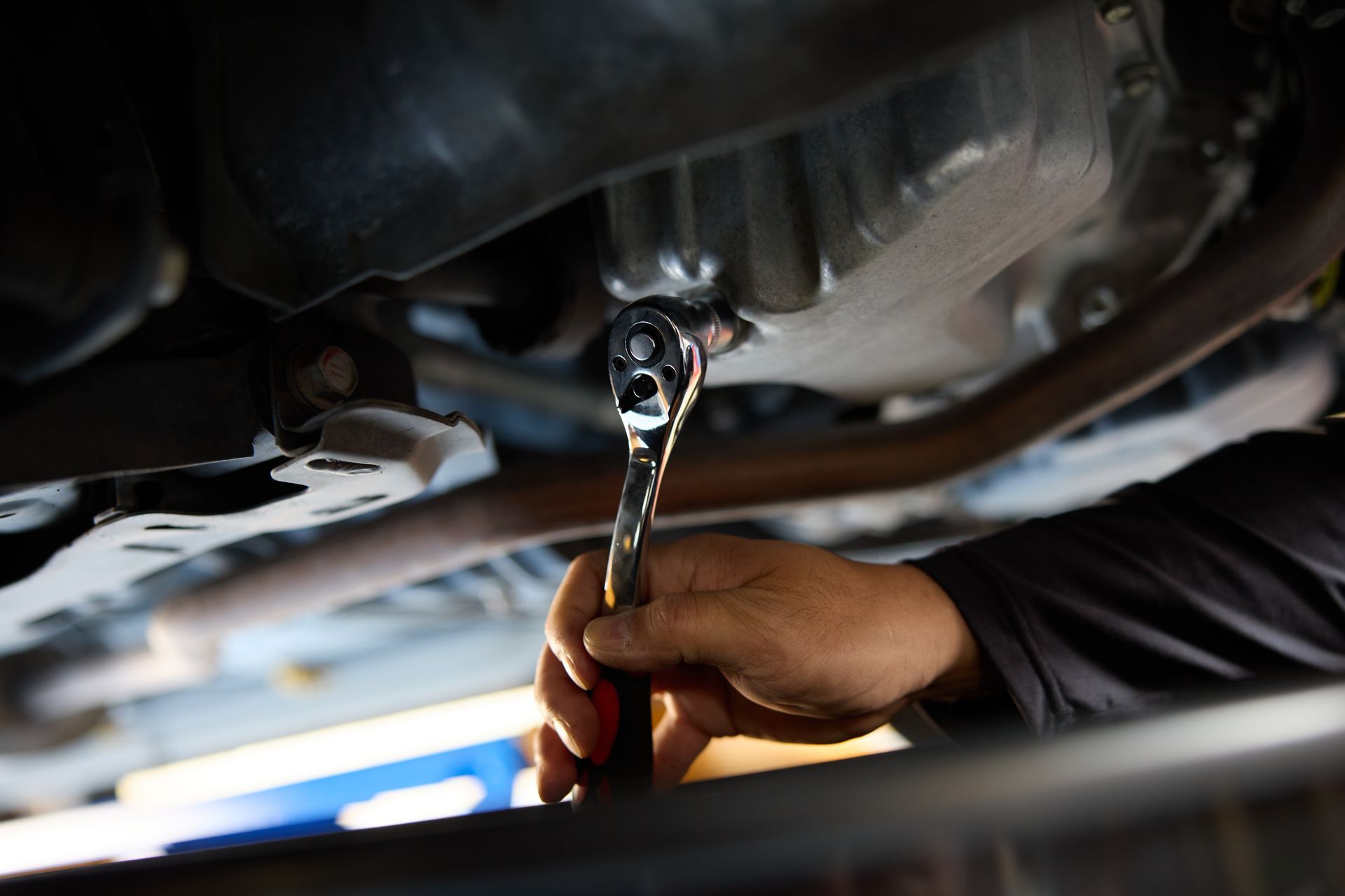 Une personne utilise une clé pour desserrer un boulon sous une voiture.