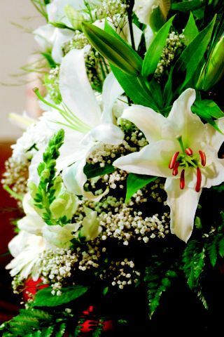 Primer plano de lirios blancos y otras flores blancas y verdes dispuestas en un ramo.