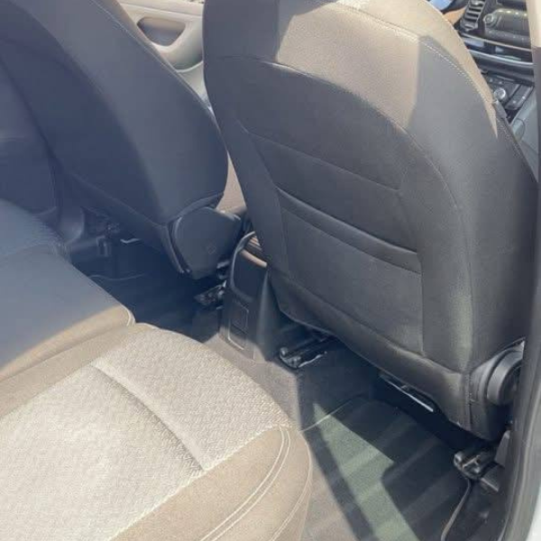 Une personne portant des gants noirs nettoie un tapis de voiture avec un nettoyeur à vapeur.