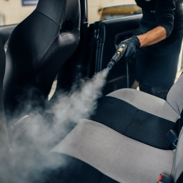 Personne nettoyant un siège de voiture avec un nettoyeur à vapeur, libérant de la vapeur.